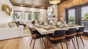 Un espace repas moderne avec une grande table dressée pour six personnes, entourée de chaises noires agrémentées d’éléments en bois.