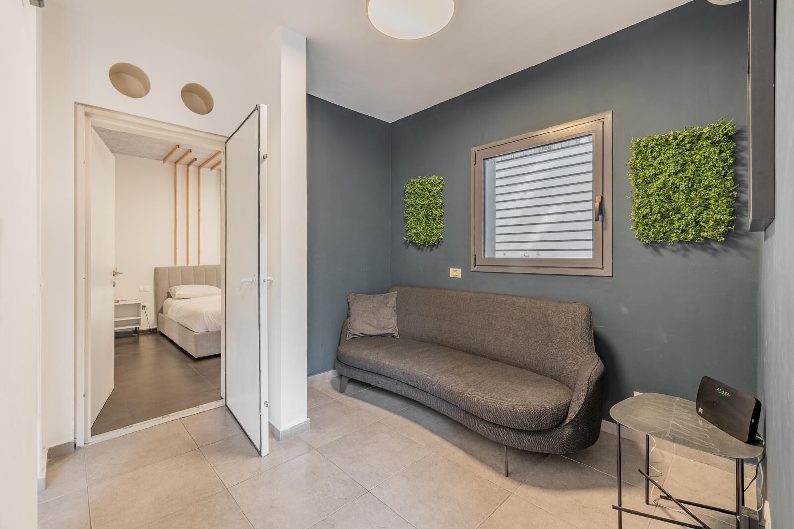 A modern living room with a grey sofa, a small table, and a window with blinds.