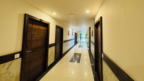A hotel corridor with wooden doors, white tiled floors, and a long hallway. - Col's Hotel Uphaar (Ujjain)