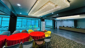 A conference room with round tables, chairs, a reception desk, and a large chandelier. - Col's Hotel Uphaar (Ujjain)