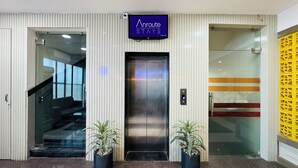 A hotel entrance with a sign reading "Anroute STAYS", an elevator, and potted plants. - Col's Hotel Uphaar (Ujjain)