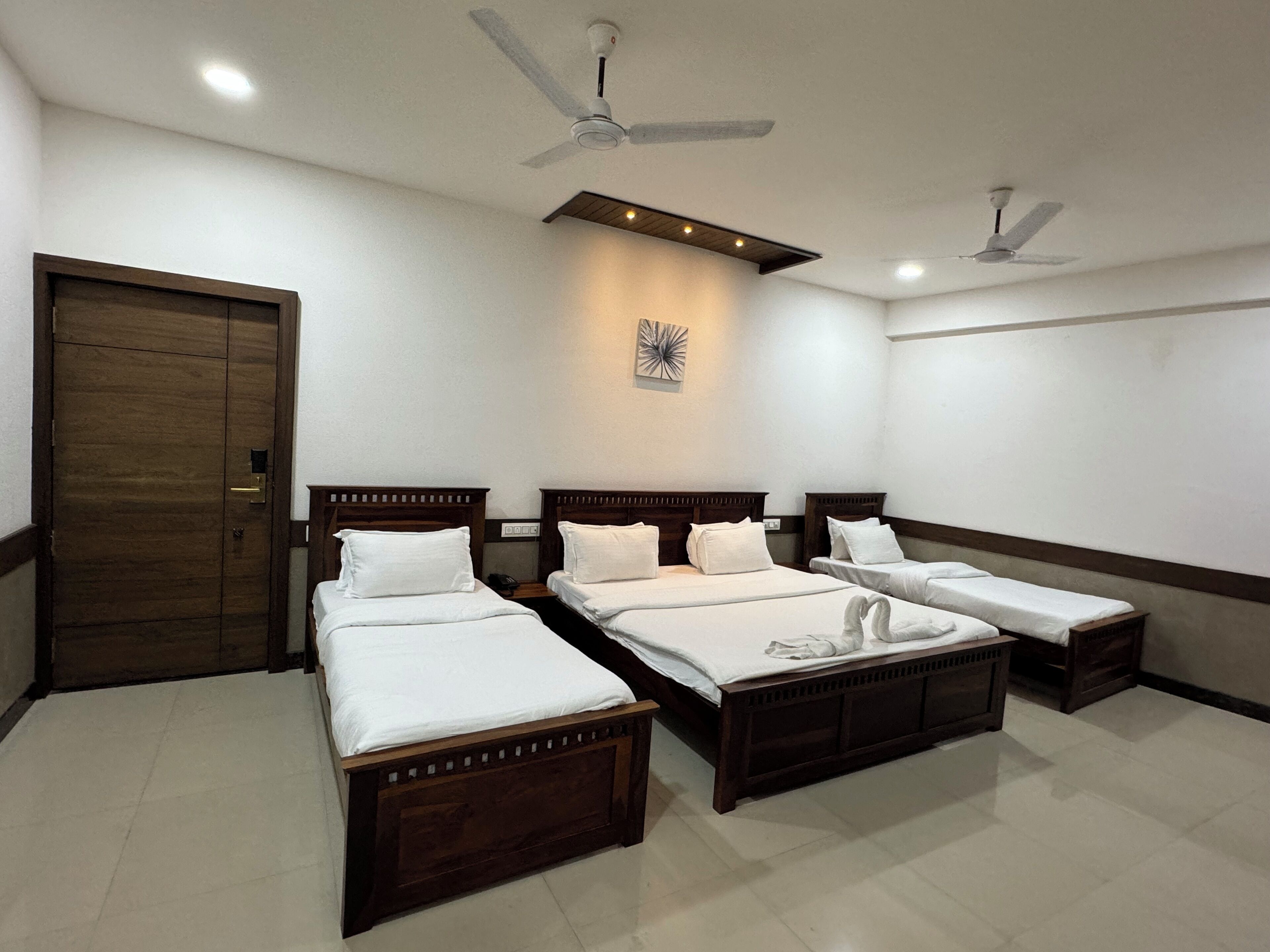 Una habitación de hotel con tres camas de madera, un ventilador de techo, iluminación empotrada y una puerta.