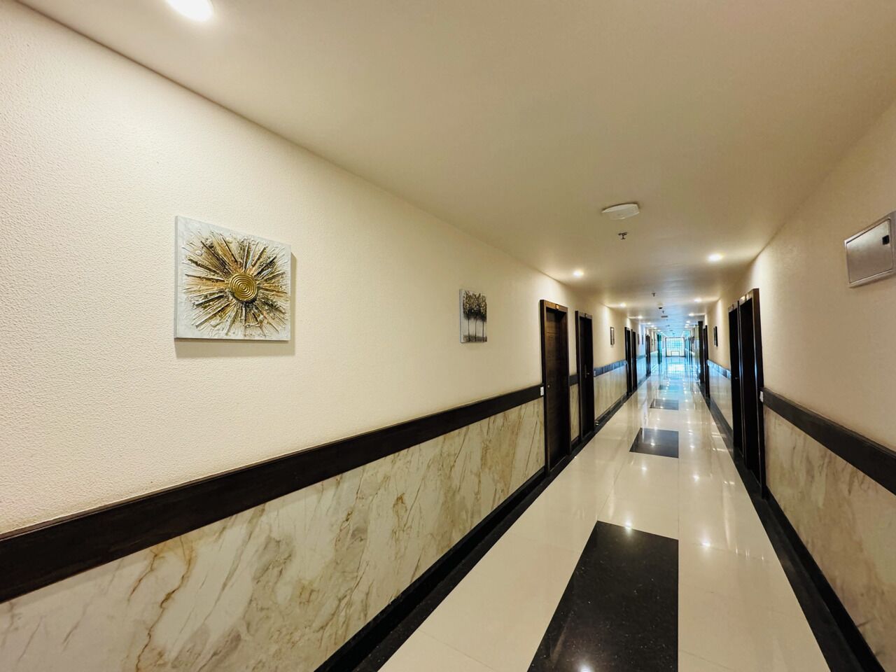 A hotel hallway with marble flooring, black and white trim, and artwork on the walls.