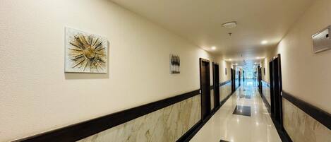 A hotel hallway with marble flooring, black and white trim, and artwork on the walls.