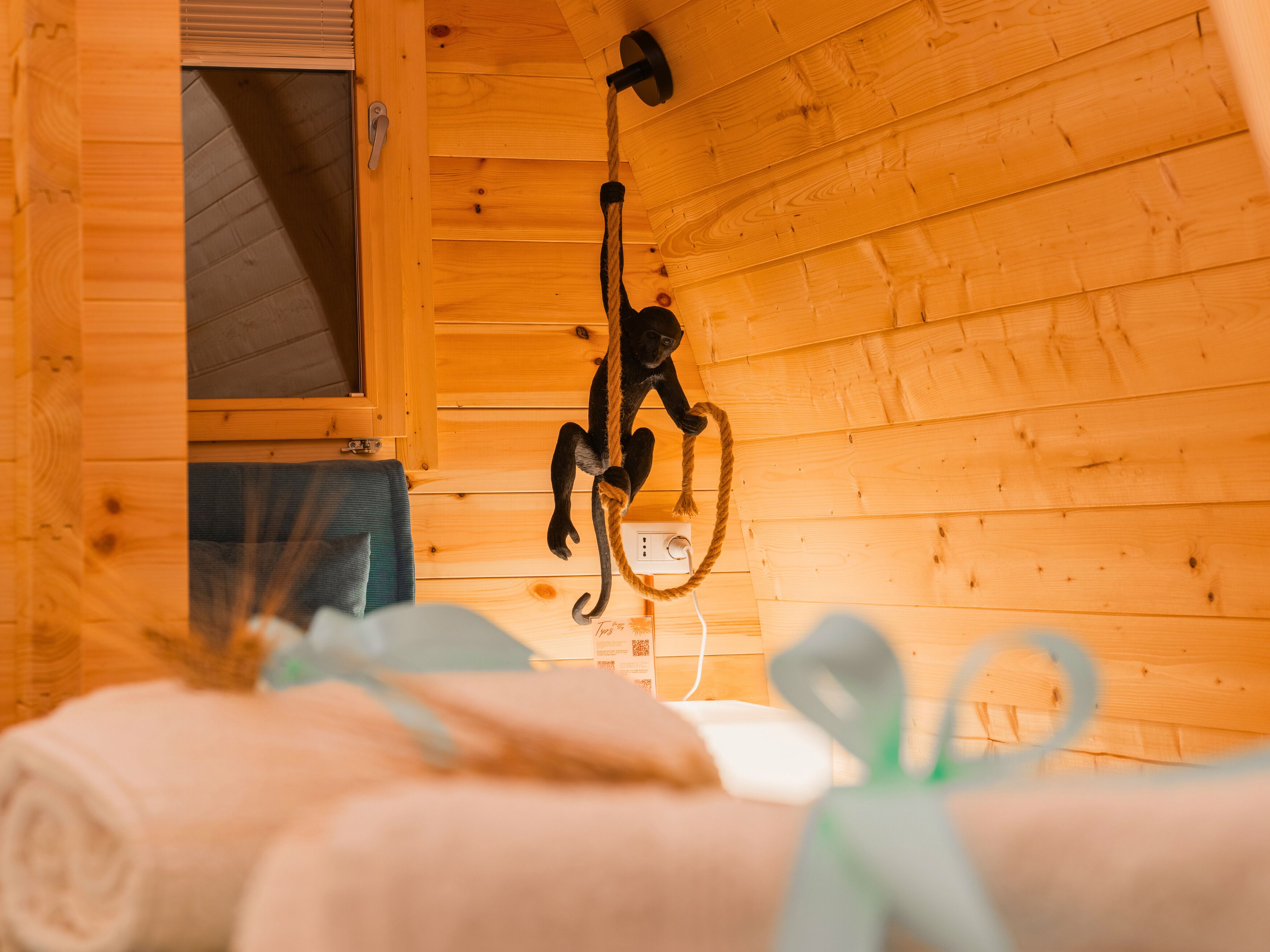 Ein Holzblockhaus-Interieur mit einer Hänge-Seil, einem Fenster und einem Bett mit aufgerollten Handtüchern.