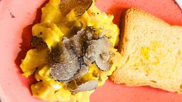 Scrambled eggs with truffle slices and toast on a pink plate.