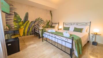 Un dormitorio con cama, mesitas de noche, un escritorio y un mural de hojas tropicales en la pared.