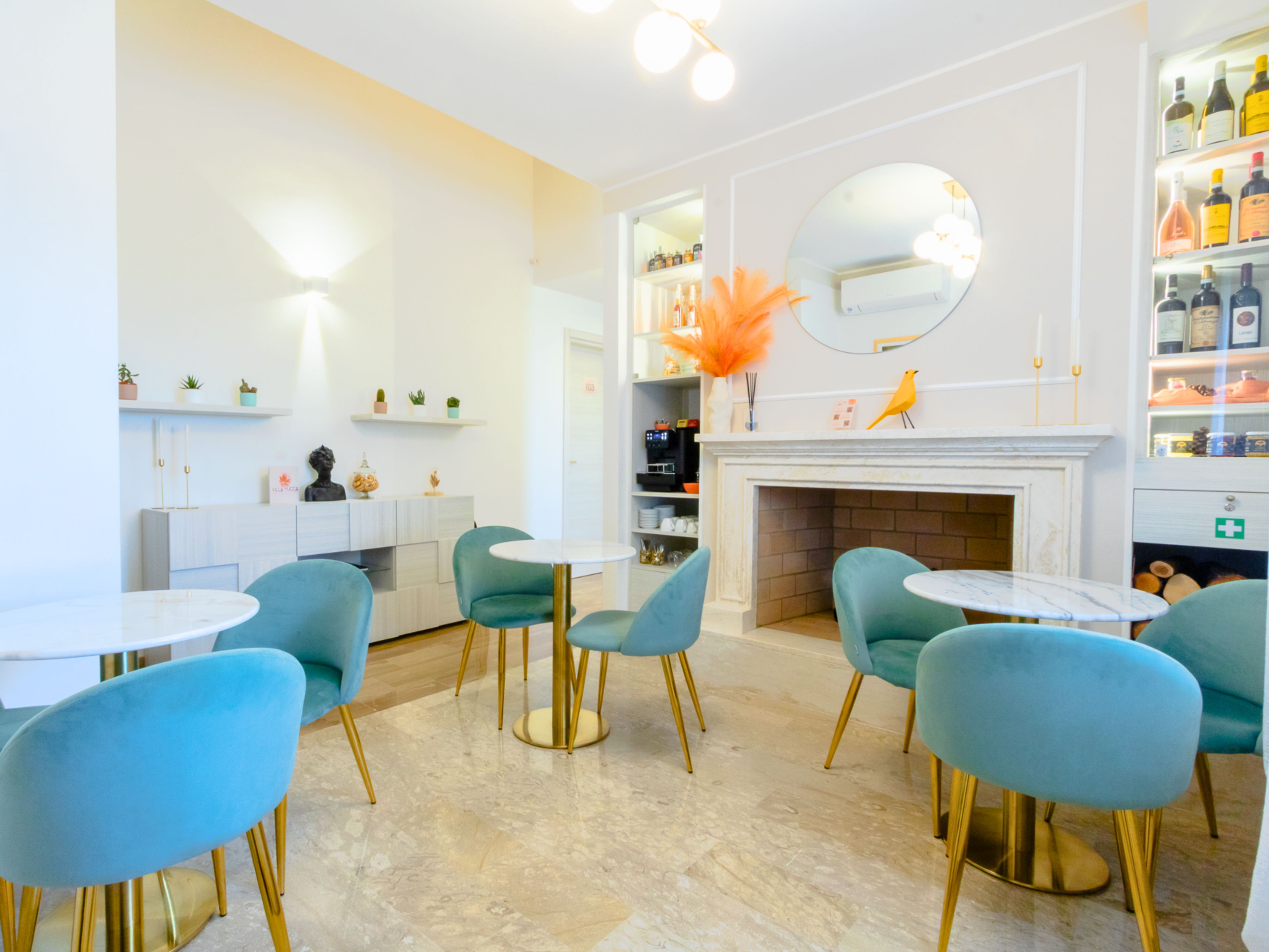 A modern interior with round tables and teal chairs, a fireplace, and a mirror above it.