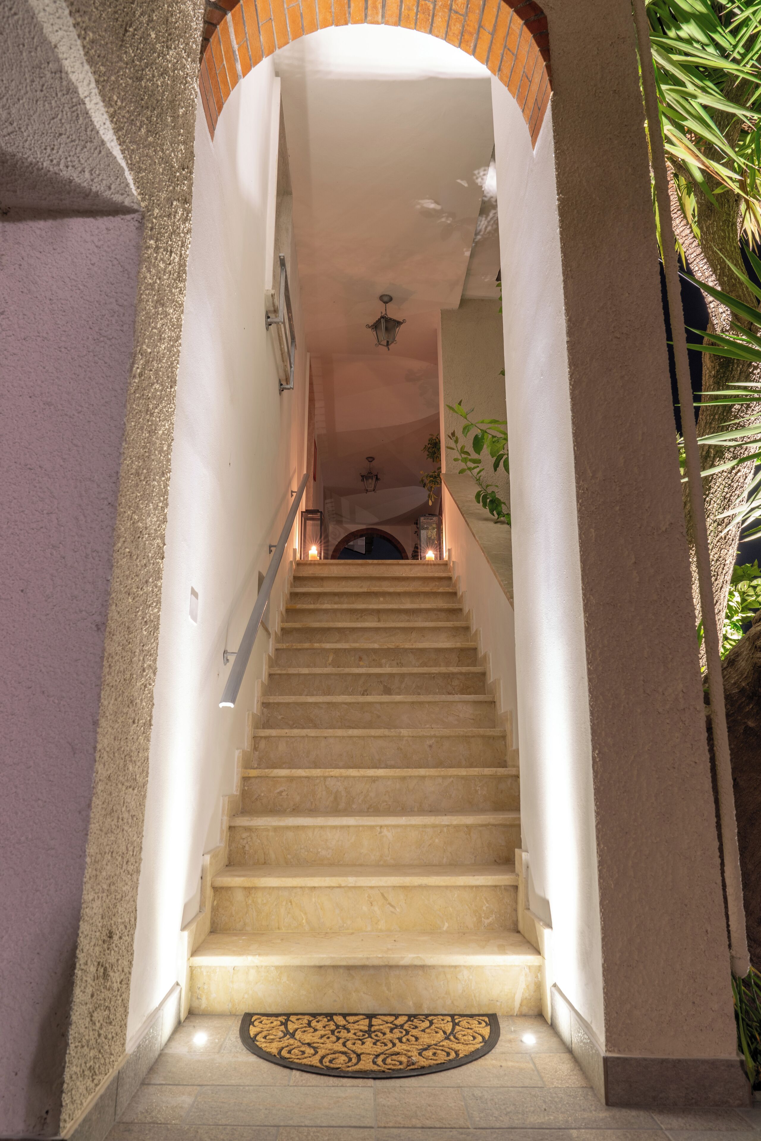 A staircase with a handrail, a doormat at the bottom, and a ceiling light fixture.