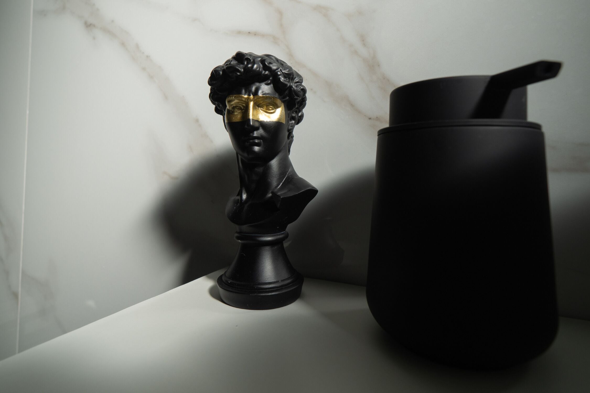 A black bust sculpture on a white surface next to a black container.