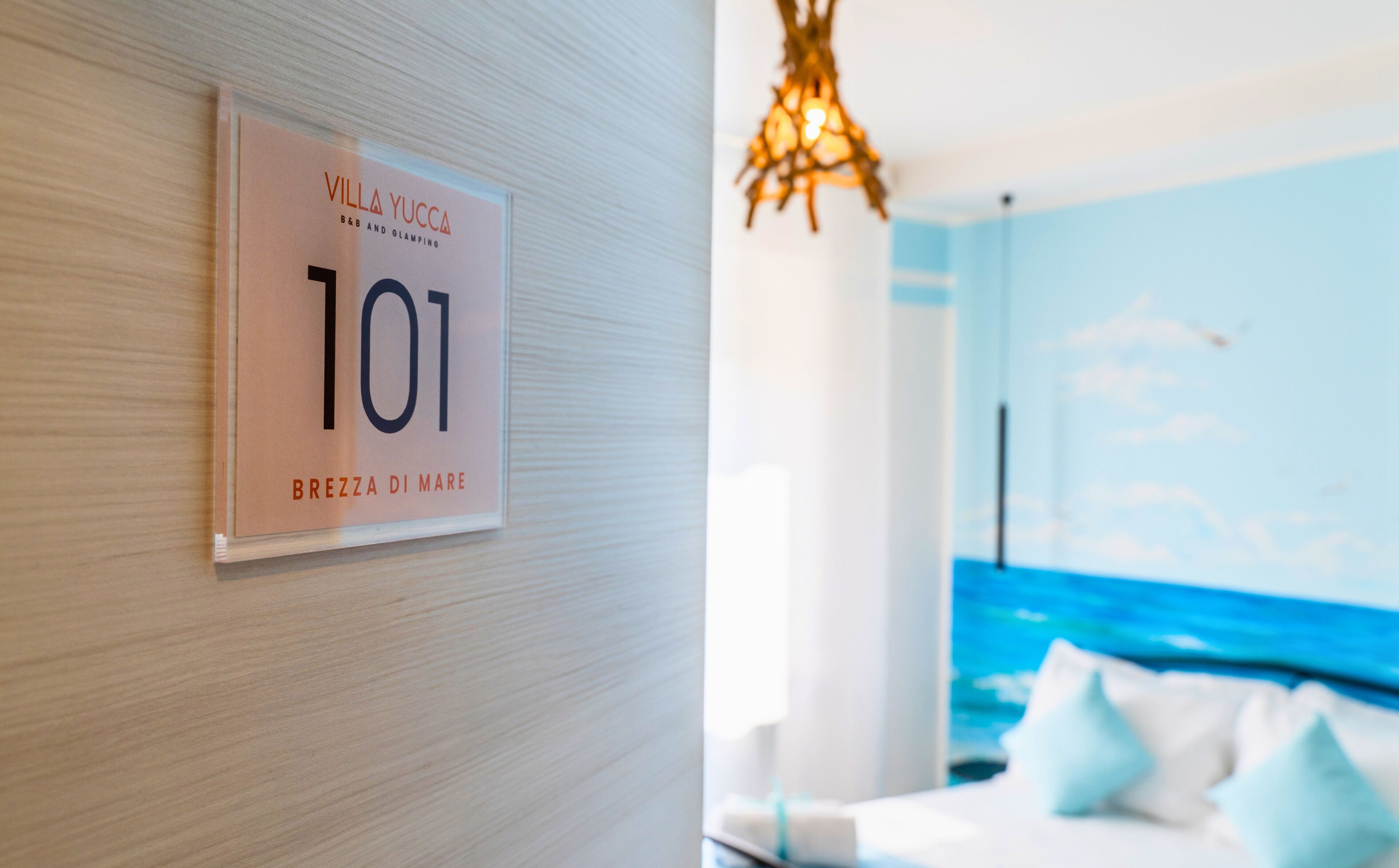 Une chambre d’hôtel avec une pancarte indiquant le numéro 101, un lit avec des oreillers et une vue sur la mer.