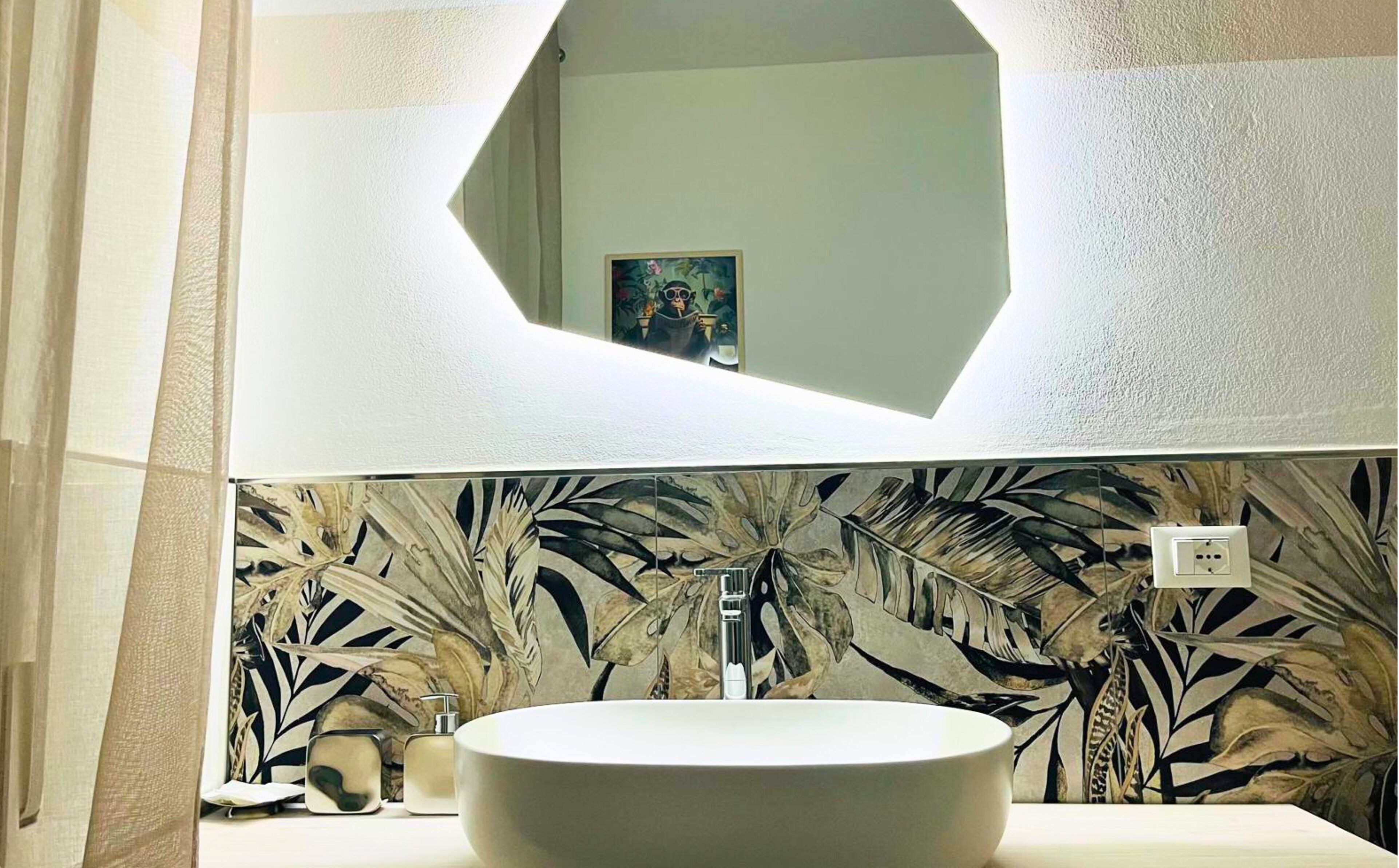A bathroom with a round sink, a mirror, and a wall with a leaf pattern.