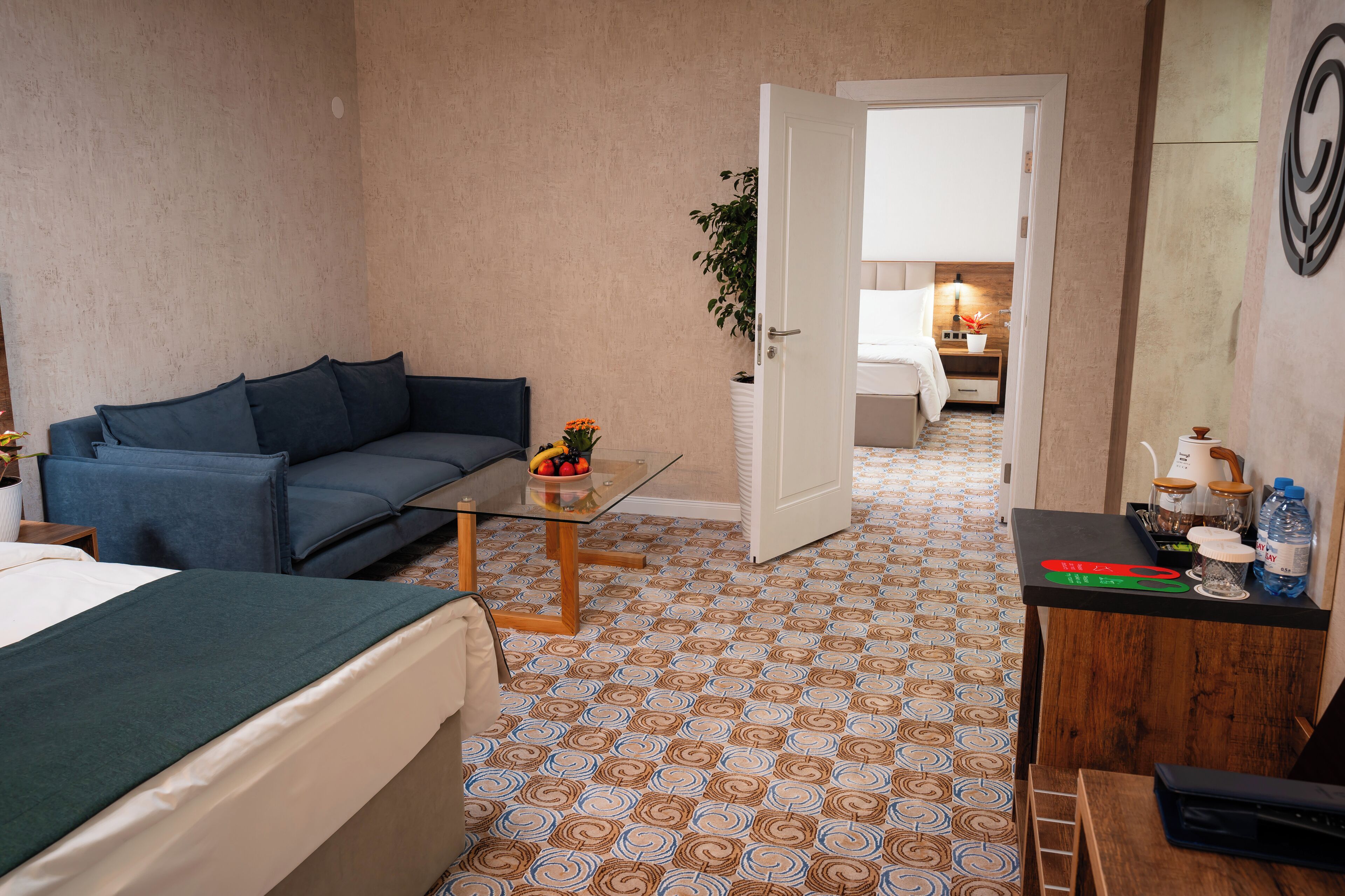 Ein Hotelzimmer mit Bett, Sofa, einem kleinen Tisch mit Pflanze, Schreibtisch mit Lampe und einem gemusterten Boden.