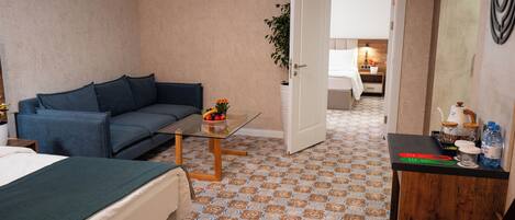 Ein Hotelzimmer mit Bett, Sofa, einem kleinen Tisch mit Pflanze, Schreibtisch mit Lampe und einem gemusterten Boden.