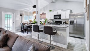 A modern kitchen with white cabinetry, a stainless steel refrigerator, and a bar area with two black bar stools.