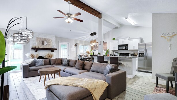 A modern living room with a sectional sofa, a dining area, and a kitchen with white cabinets and stainless steel appliances.