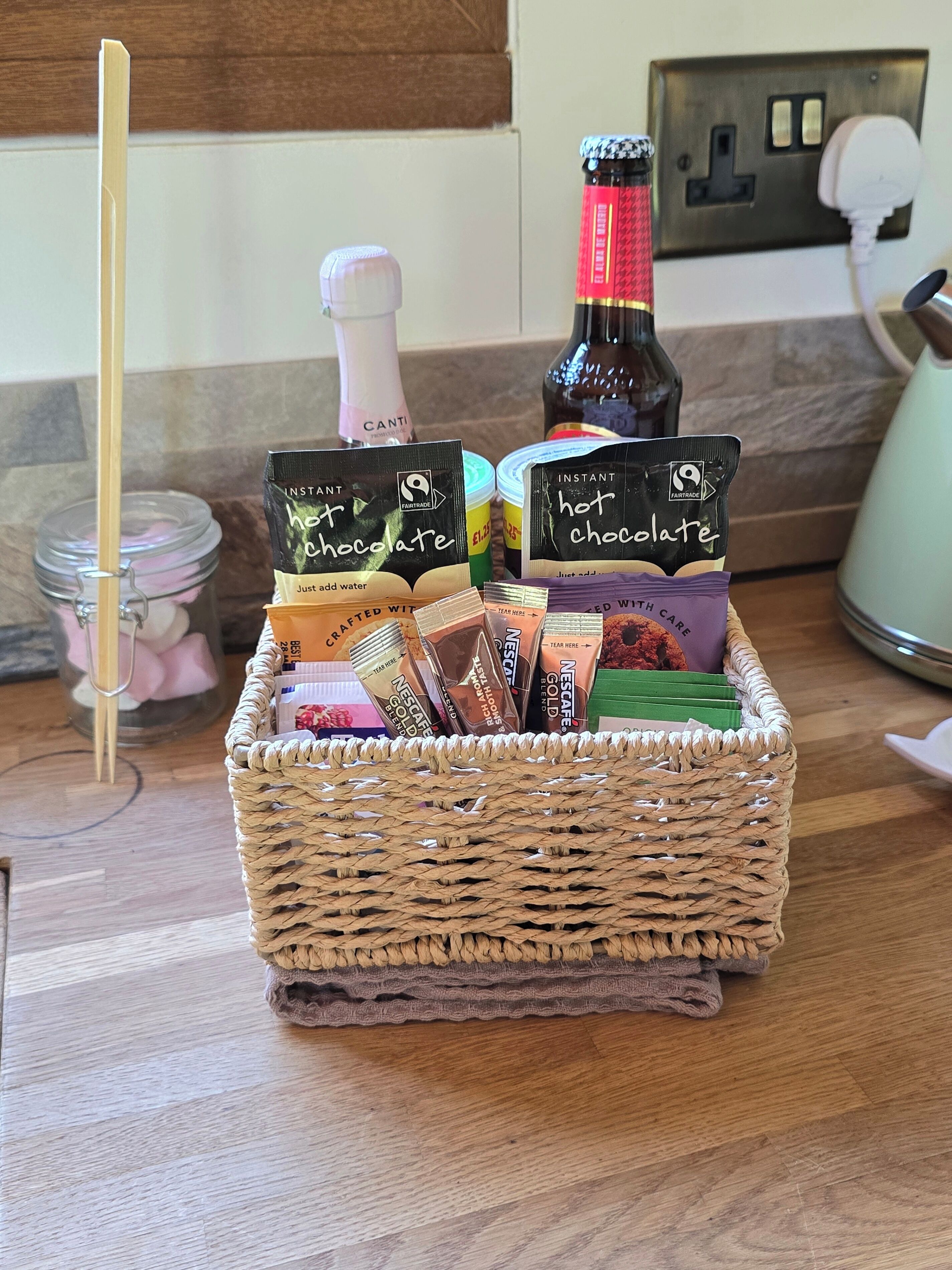 A wicker basket filled with instant hot chocolate and Nescafé Gold Blend coffee packets on a kitchen counter.