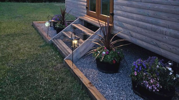 A wooden cabin with a glass door, a small porch with steps, and potted plants.