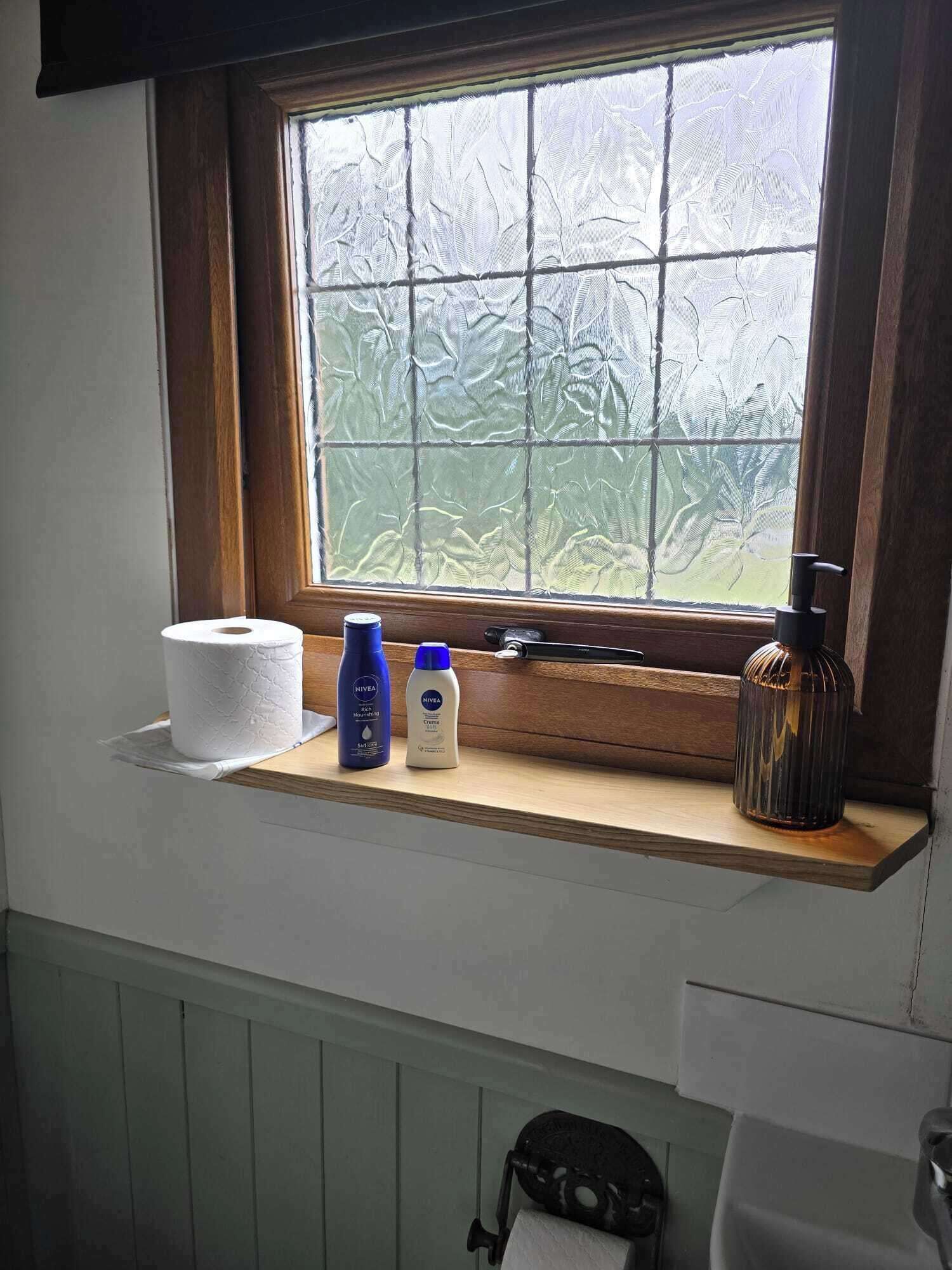 A bathroom with a window, a toilet paper roll, two Nivea products, and a soap dispenser on a wooden ledge.