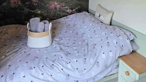 A bedroom with a curved ceiling, a bed with a patterned duvet, a nightstand, a wall-mounted lamp, and a scenic view of a landscape.
