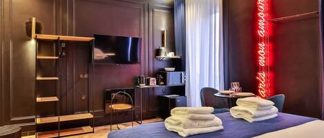 A hotel room with a bed, a TV, a desk with a chair, a microwave, and a neon sign.
