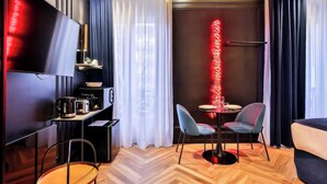 Une chambre d’hôtel moderne équipée d’un téléviseur à écran plat, d’une petite kitchenette, d’un coin repas avec deux chaises et d’un néon mural.