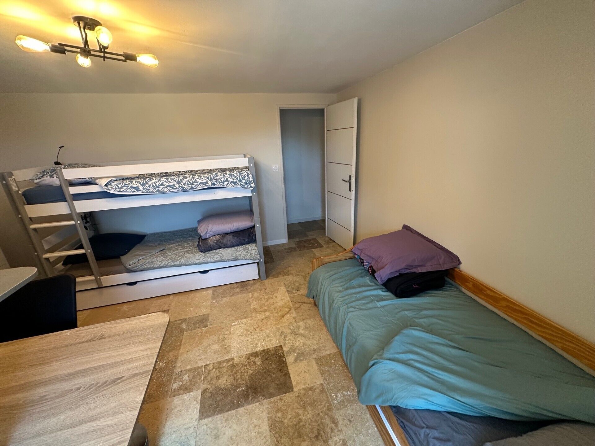 A bunk bed with a desk and chair, a single bed with a pillow, and a wardrobe.
