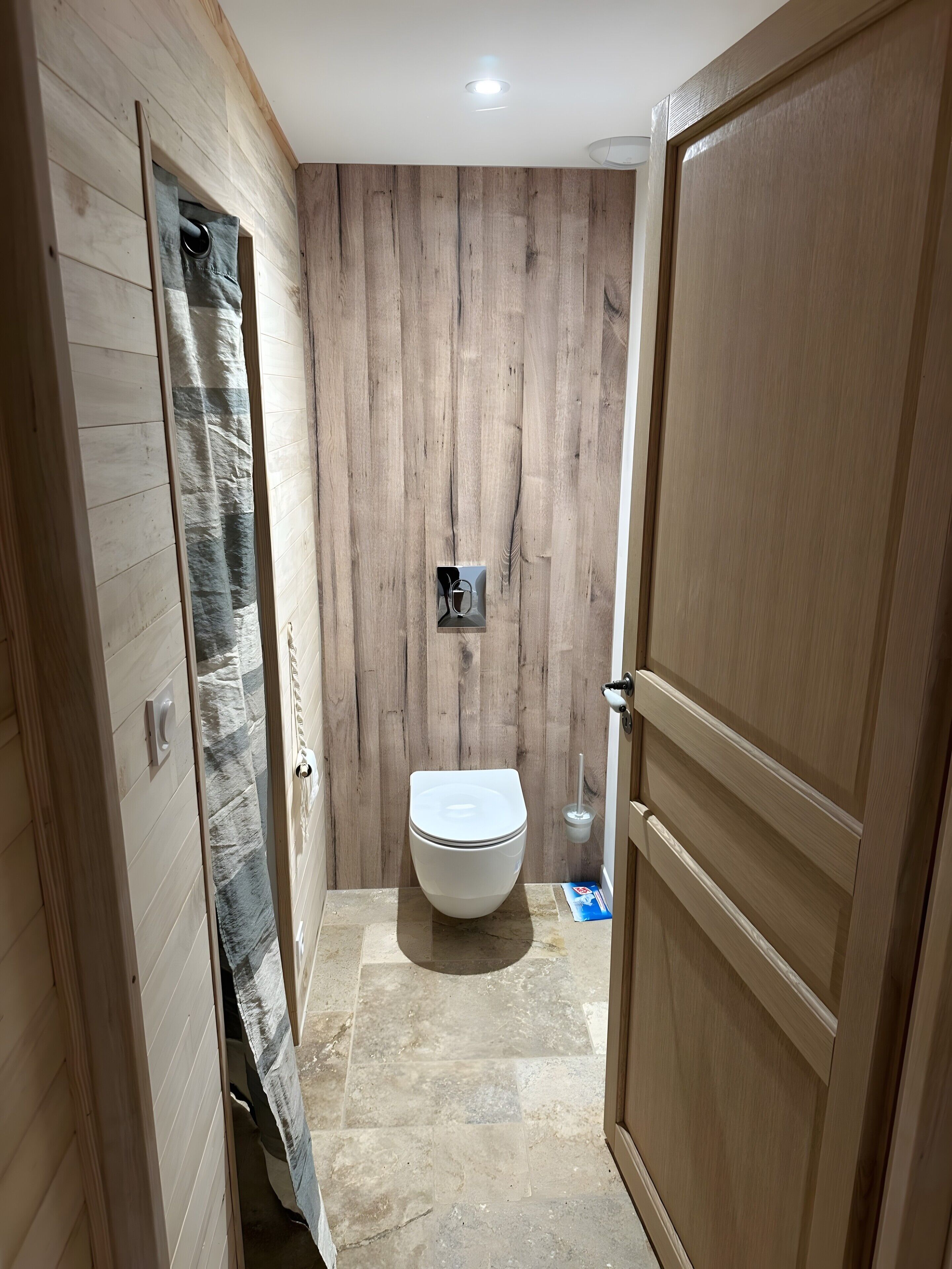 A bathroom with a wooden wall, a toilet, and a shower curtain.
