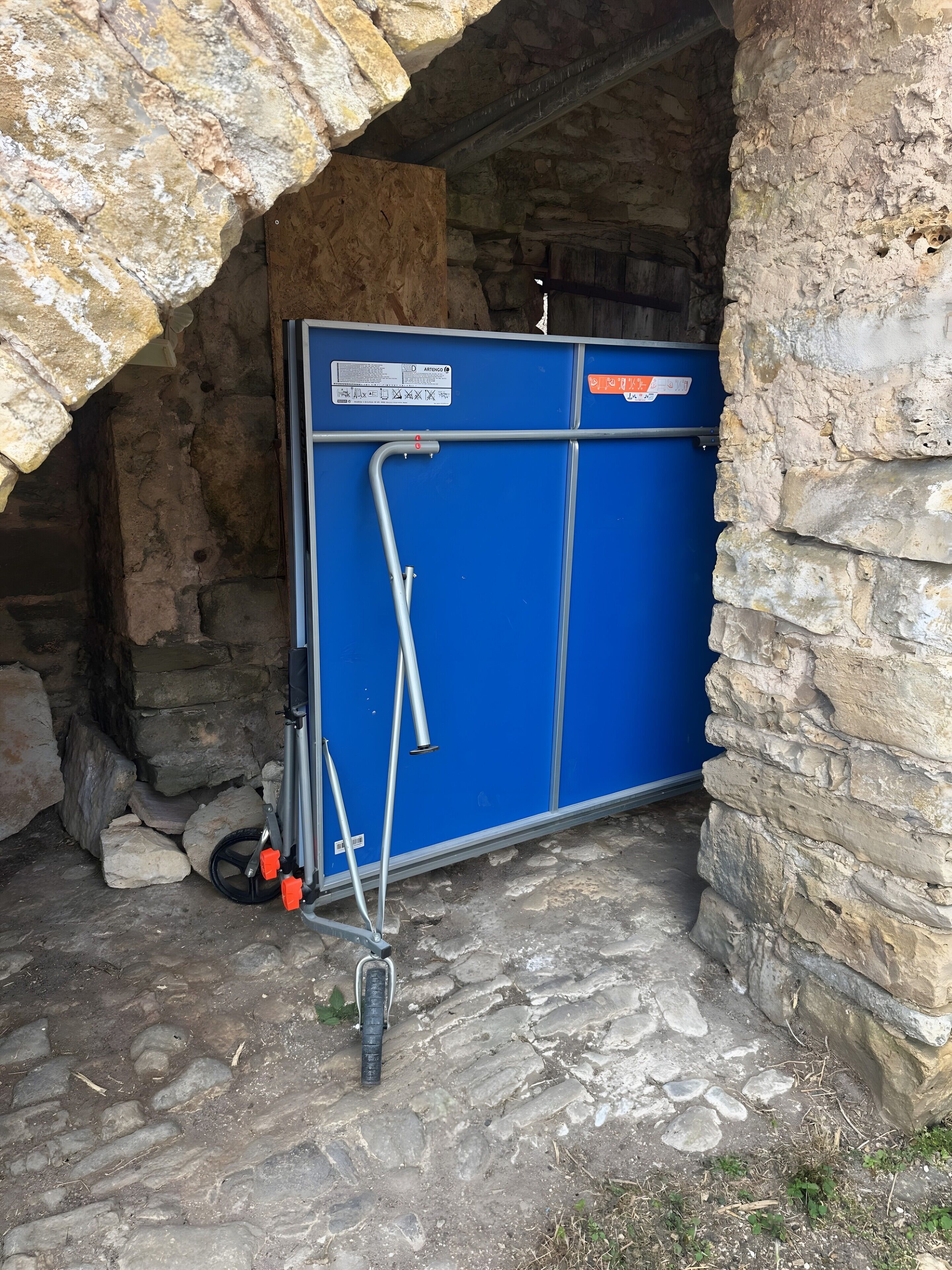 A blue metal gate with a label, a metal frame, and a wheelbarrow with a wheel.