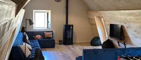 An attic room with a blue sofa, a black bean bag, a TV on a stand, and a fireplace.