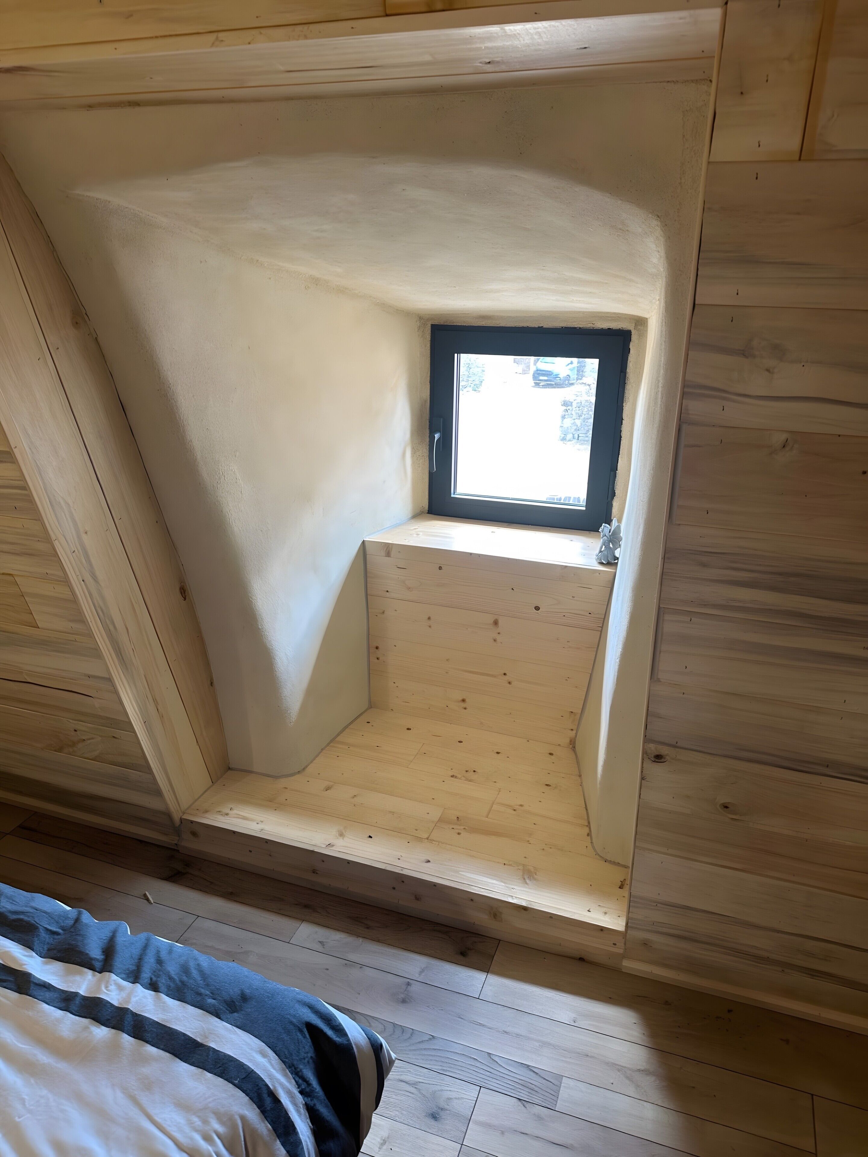 A room with a sloped ceiling, a small window, and a wooden floor.