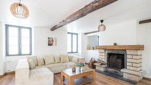 A living room with a wooden floor, a beige sectional sofa, a wooden coffee table, a fireplace, and exposed wooden beams. - Beautiful family house sleeps 9 near the castle in Dampierre (Dampierre-en-Yvelines)