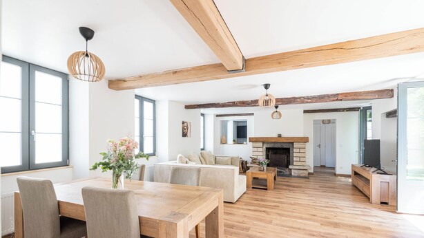 Un vaste salon doté d’un plancher en bois, d’une cheminée, d’un canapé et d’un coin repas avec une table et des chaises.