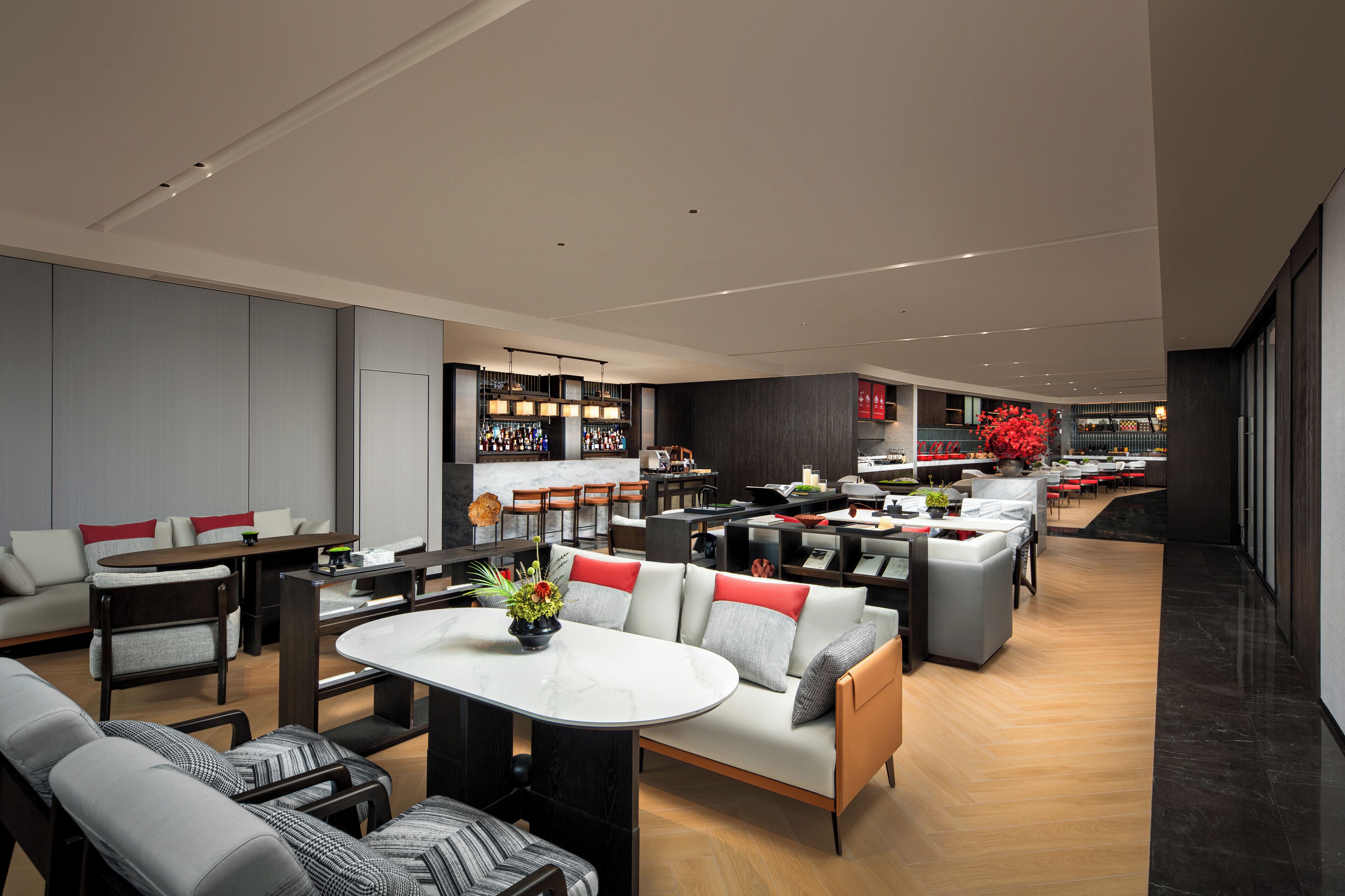 A modern hotel lobby with a seating area, a bar, and a kitchen in the background.