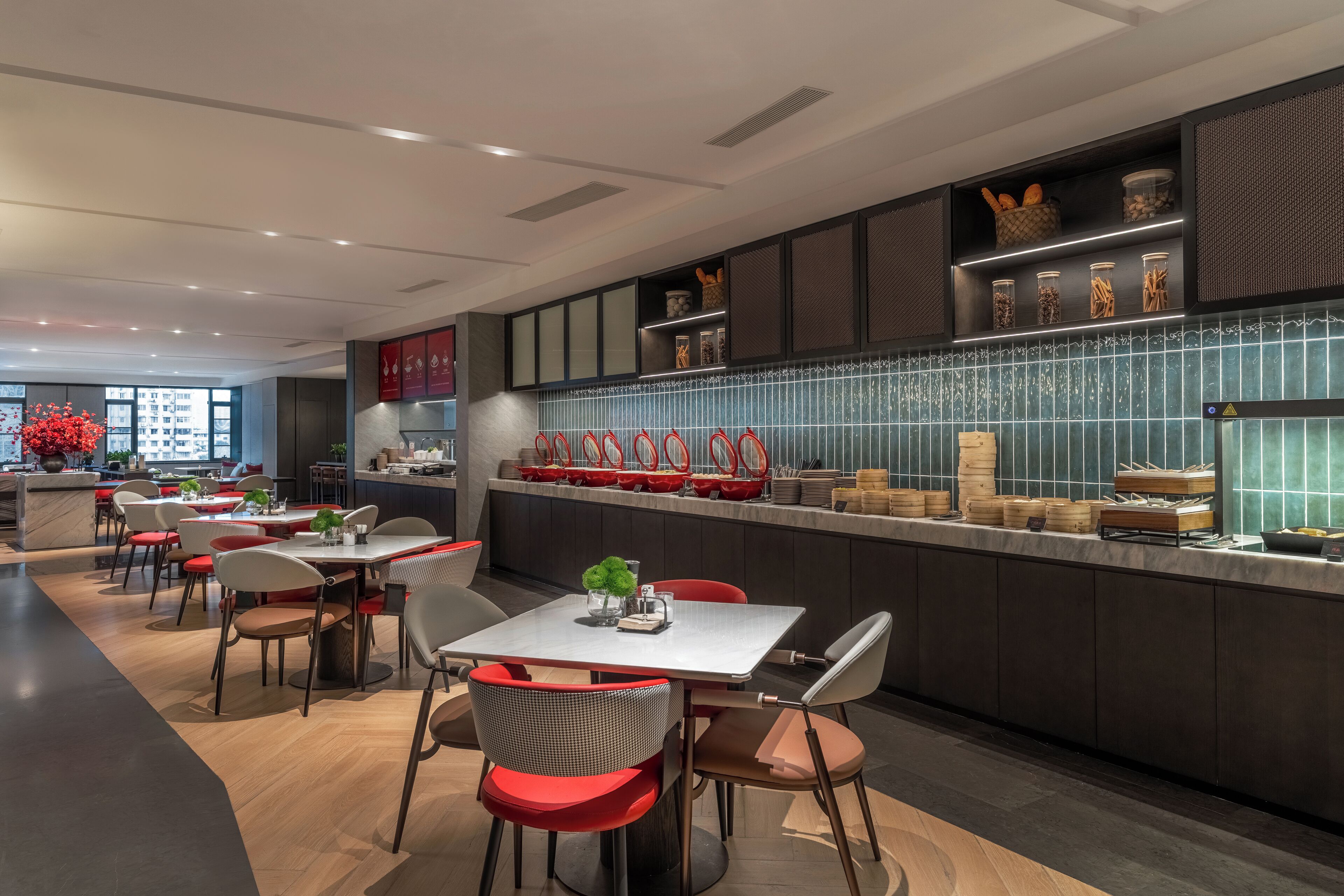 A modern restaurant with a long counter, red chairs, and a variety of food items displayed on shelves.