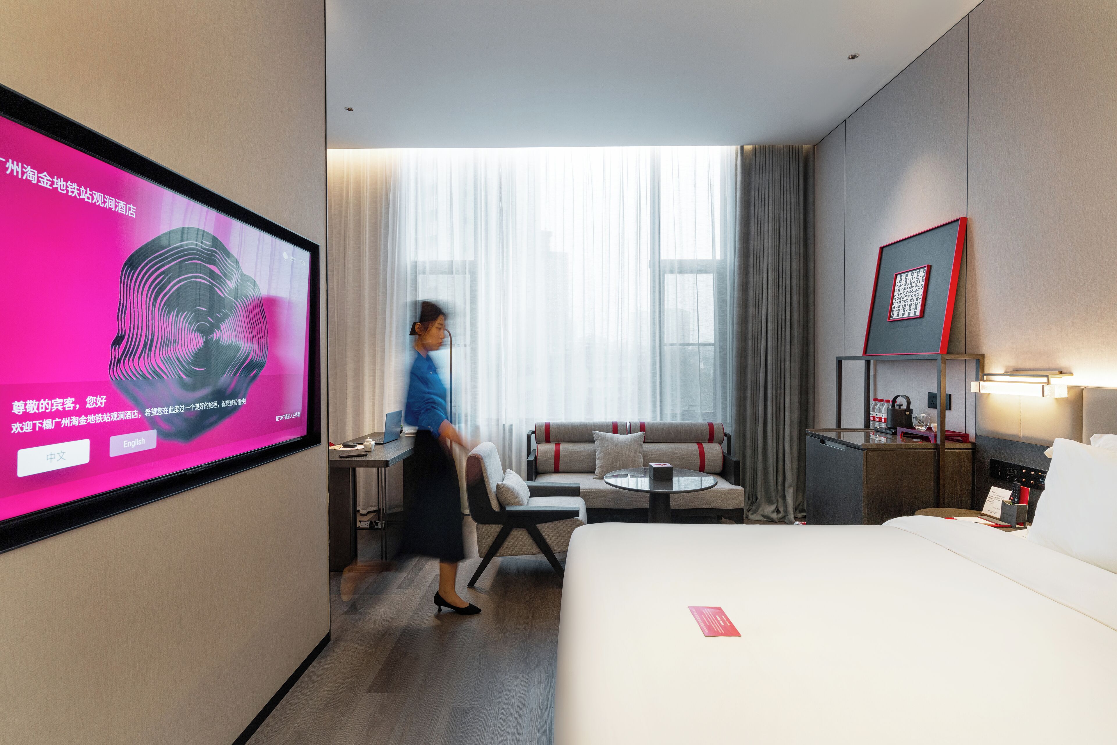 Habitación de hotel con cama, escritorio, silla, sofá, televisor y ventana con cortinas.