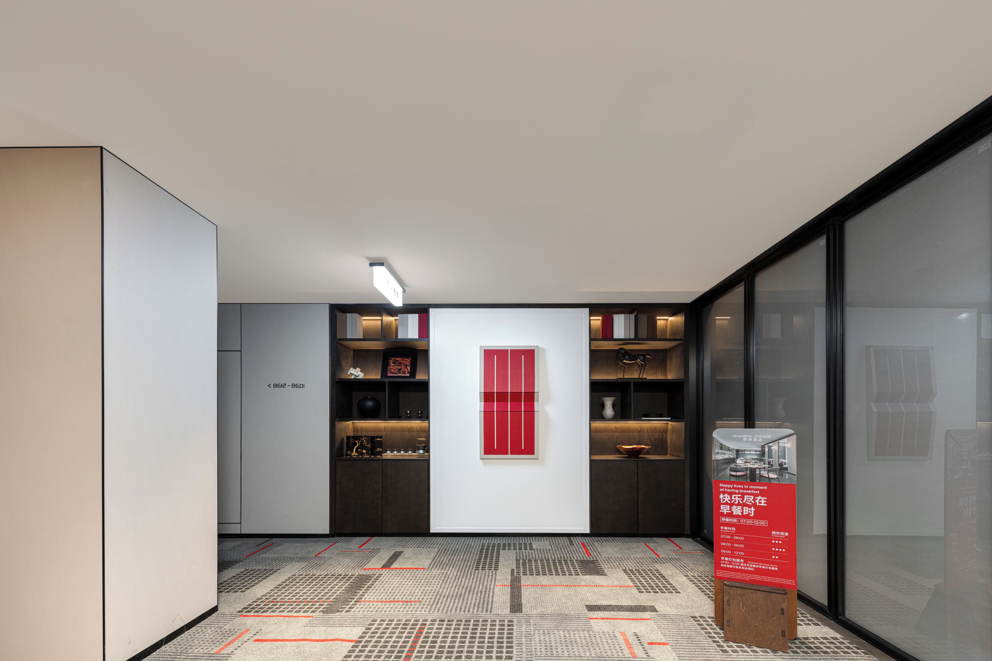 A modern hotel corridor with a patterned floor, a red accent wall, and a signboard.