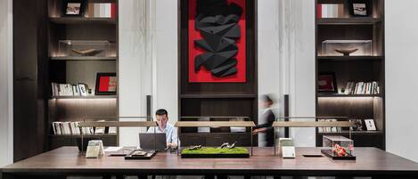A modern office space with a long table, multiple chairs, and a person working on a laptop.