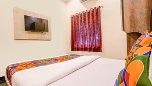 A bedroom with a bed, a TV mounted on the wall, and a window with a curtain. - Hotel Priceless (Mumbai)