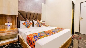 A hotel room with a bed, a nightstand, a wall-mounted shelf, and a door. - Hotel Priceless (Mumbai)
