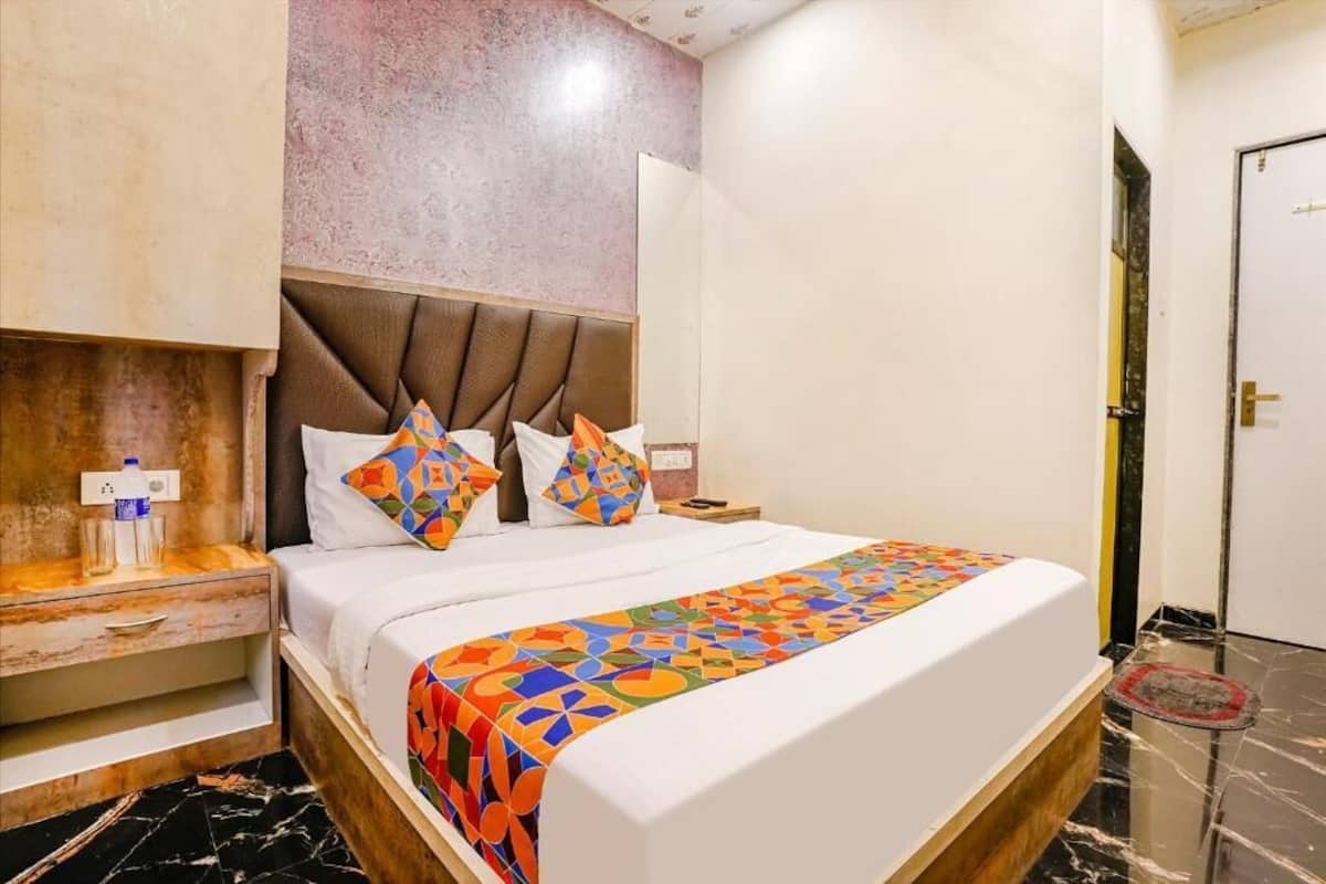 A hotel room with a bed, a nightstand, a wall-mounted shelf, and a door.