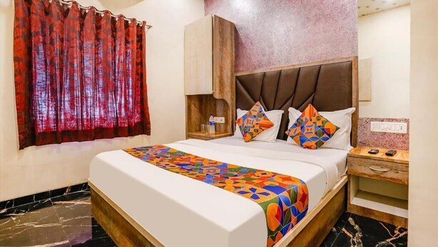 A hotel room with a bed, a nightstand, a mirror, and a window with curtains. - Hotel Priceless (Mumbai)