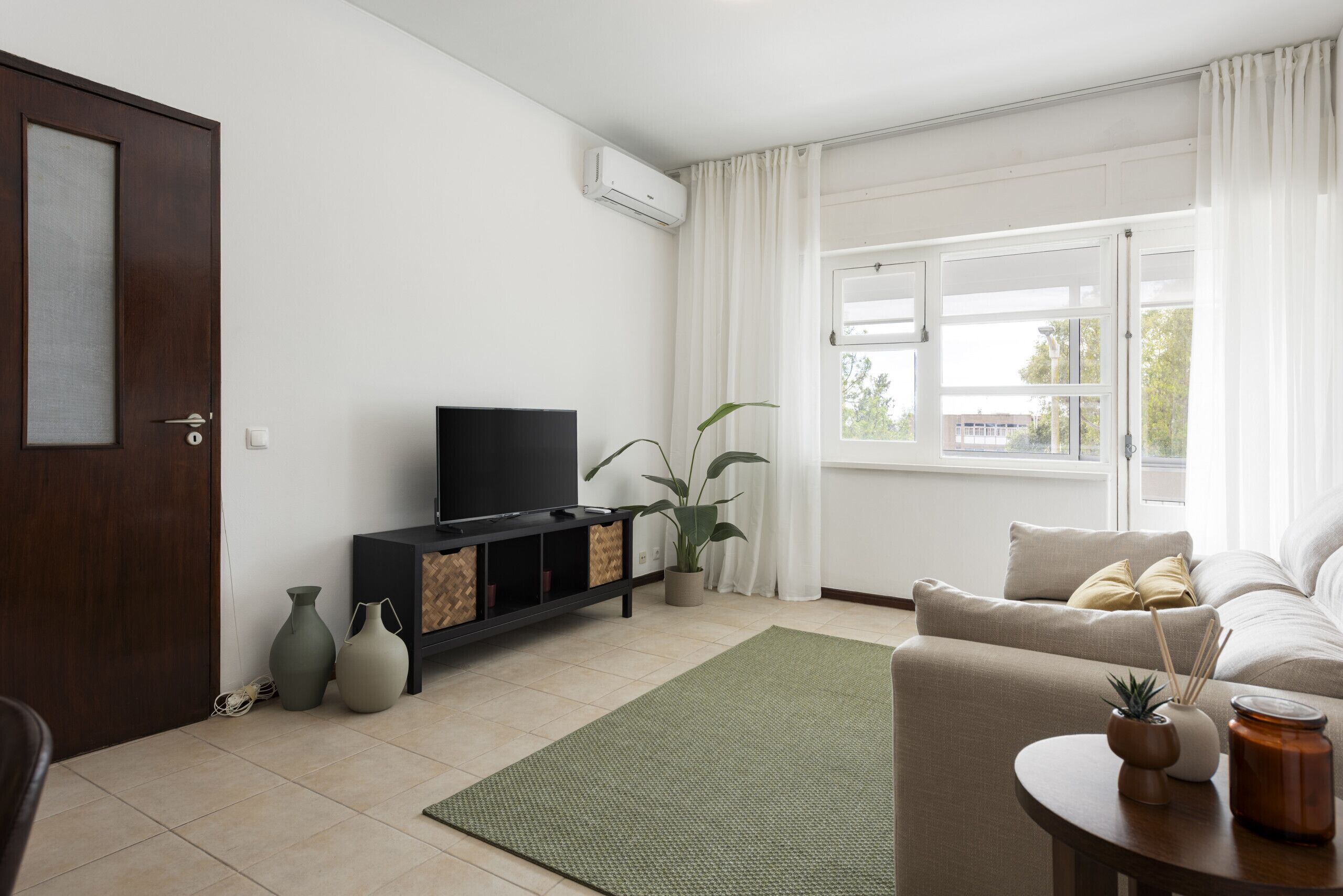 Una sala de estar con televisión, sofá y un ventanal amplio.