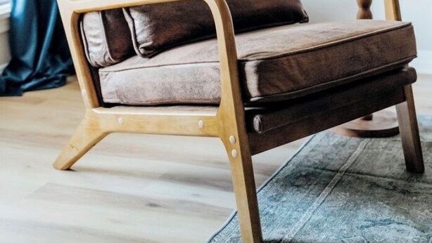 Una poltrona in pelle marrone con struttura in legno, un cuscino coordinato e un piccolo tavolino in legno.