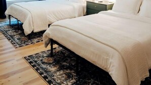 Camera d'albergo con due letti, una ventola a soffitto, un comodino e un'ampia finestra con tende.
