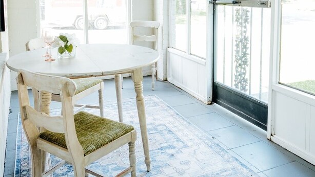 Une pièce avec une table ronde, deux chaises, une fenêtre donnant sur un camion U-Haul et un tapis à motifs.