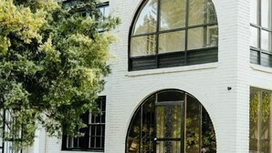 Une maison moderne aux murs en briques blanches, dotée de grandes fenêtres en arc de cercle et d’une pelouse bien entretenue.