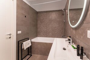 Ein modernes Badezimmer mit einer Badewanne, einem großen Spiegel und einem weißen Waschbecken.