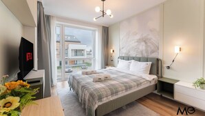 A modern hotel room with a large bed, a TV, a desk with a plant, and a view of the city. - MoHost - Uno (Brasov)