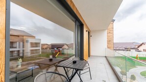 A balcony with a glass railing, a wooden table, and a chair. - MoHost - Uno (Brasov)